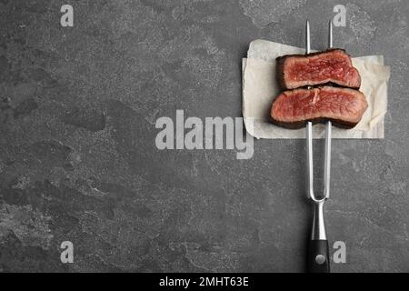 Carving fork with slices of delicious beef steak on grey table, top view. Space for text Stock Photo