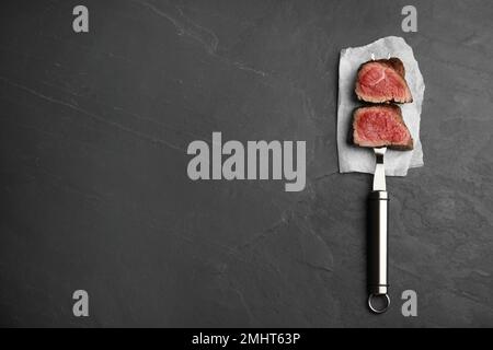 Carving fork with slices of delicious beef tenderloin on black table, top view. Space for text Stock Photo