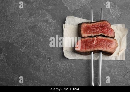 Carving fork with slices of delicious beef steak on grey table, top view. Space for text Stock Photo