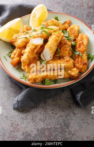 Battered and fried golden squid strips with lemon closeup on the plate on the table. Vertical Stock Photo