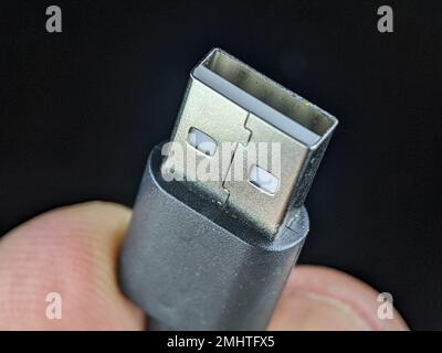 Closeup finger holding USB charger cable on a black background. Stock Photo