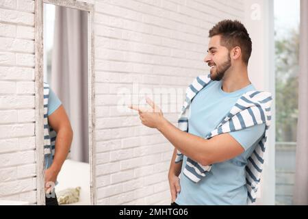 Young man looking at himself in large mirror at home Stock Photo