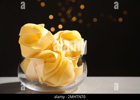 Uncooked pappardelle pasta on grey table against blurred lights Stock Photo