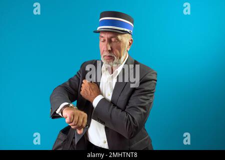 The train conductor looks at his wristwatch. Portrait of a train controller on a blue background. Stock Photo