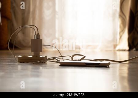 Charging the phone from an extension cord on the floor in the apartment, charging the phone Stock Photo