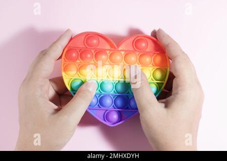 Colorful Antistress Pop it toy. Rainbow sensory fidget isolated on pink background, in the hands during the game. New trendy silicone toy. Toy for the Stock Photo