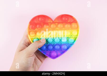 Colorful Antistress Pop it toy. Rainbow sensory fidget isolated on pink background, in the hand during the game. New trendy silicone toy. Toy for the Stock Photo