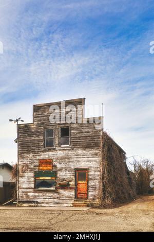 Front view of an old abandoned square unpainted wood planked store front with an orange door Stock Photo