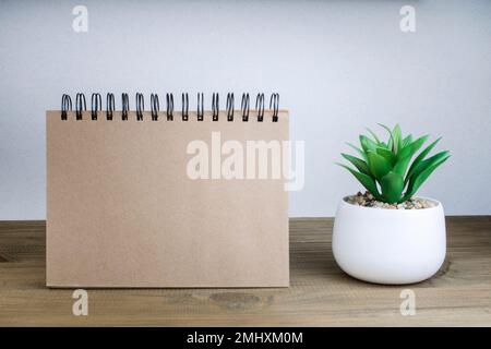 An open notebook with blank pages next to a green plant in a pot on a wooden table. Copy space. Retro style. Stock Photo