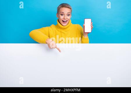 Photo of astonished positive lady stand behind empty space presenting novelty new smartphone iphone isolated on blue color background Stock Photo