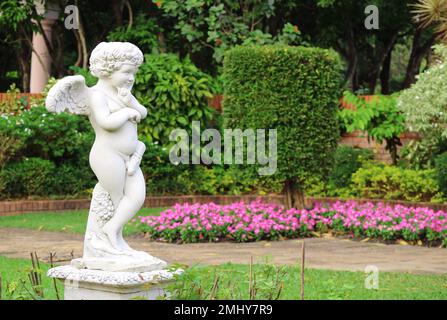 An adorable cupid sculpture in the flowering garden Stock Photo