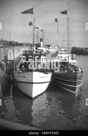 1950, historical, a large no of holiday makers at the harbour at Bridlington, East Yorkshire, England, UK, boarding the waiting pleasure boats, including 'Boys Own' and the Bridlington Queen. On the boat, Bridlington Queen, which has a sign saying 2's (shillings in old money) Cruise Now. Built in 1938, Boys Own was one of five excursion vessels at Bridlington, known as 'the Belles of the North Sea'. Stock Photo