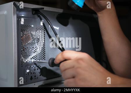 Repairman with flashlight fixing microwave oven indoors, closeup Stock Photo