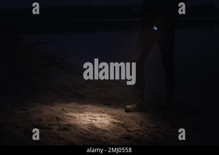 Man with flashlight walking near river at night, closeup Stock Photo
