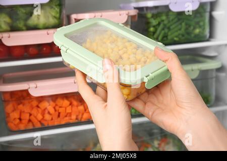 https://l450v.alamy.com/450v/2mj05x8/woman-putting-container-with-corn-in-refrigerator-with-frozen-vegetables-closeup-2mj05x8.jpg