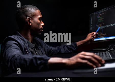 Black male reading written code on monitor in dark room Stock Photo