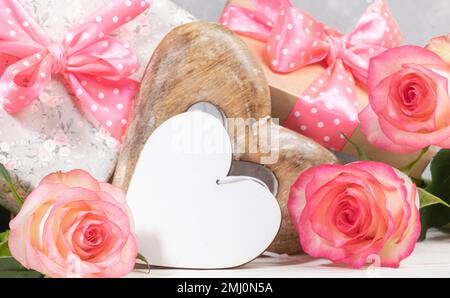Gift boxes with pink polka dots bows, gentle peach color roses, empty white wooden heart with space for text. Composition on Valentine's day, mother's Stock Photo