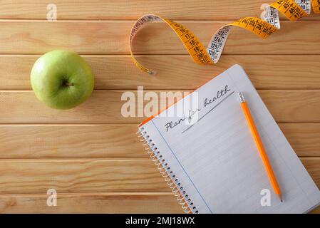 Health plan with notebook and pencil on wooden table with apple and tape measure. Top view. Stock Photo