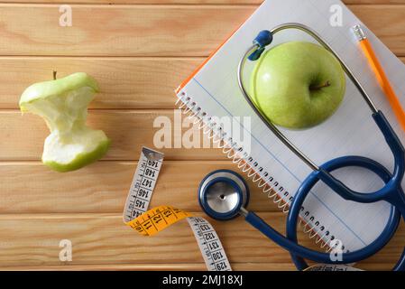 Weight control and healthy lifestyle with notebook and pencil on wooden table with apple, tape measure and stethoscope. Top view. Stock Photo