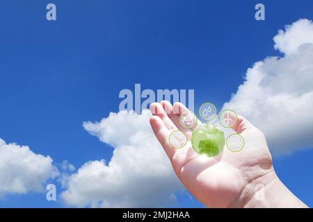 Hand holding green globe with eco energy icon on blue sky with white clouds background, Clean energy concept Stock Photo