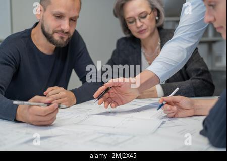Four colleagues are discussing blueprints in a conference room in an office. Brainstorming of engineers and architects. Stock Photo