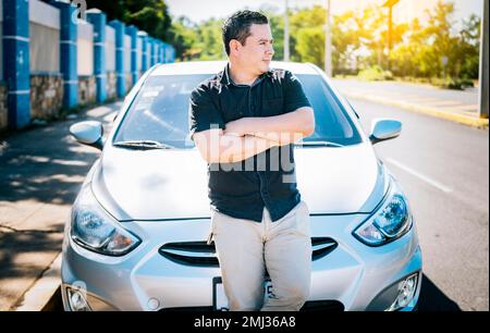 Portrait of smiling man leaning on the car. Young man with crossed arms leaning on his car. Handsome young man with arms crossed leaning on his car Stock Photo