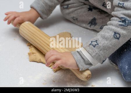 Boy kneading cookie dough with a wooden rolling pin and his brothers and mothers hands in the background Stock Photo