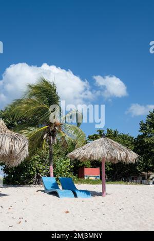 Plastic lounge chairs and palm leaf parasols on the beach at Playa Ancon near Trinidad, Cuba Stock Photo