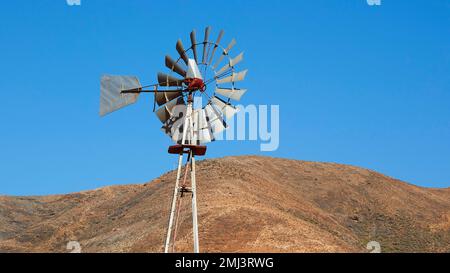 Wind turbine, irrigation, brown hill, blue cloudless sky, Vega Rio Las Palmas, island interior, Fuerteventura, Canary Islands, Spain Stock Photo