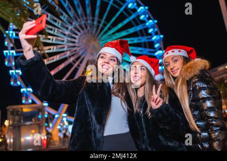 Christmas in the city at night, decoration in winter. Friends on an illuminated Ferris wheel taking a selfie with the phone Stock Photo