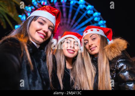 Christmas in the city at night, decoration in winter. Friends on an illuminated Ferris wheel taking a selfie Stock Photo