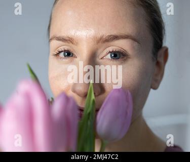 A girl with blue gases looks directly into the camera and holds a bouquet of pink tulips in her hands. Stock Photo