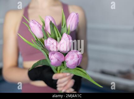 Girl boxer with bandaged hands holds seven tulips, women's sport, gentle boxing Stock Photo