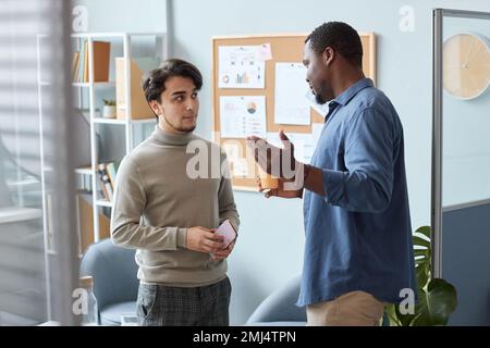 Waist up portrait of two men wearing casual clothes chatting in office setting Stock Photo
