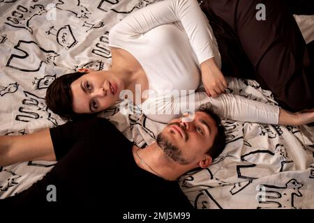 Beautiful couple are lying on the bed and looking at the camera. Young couple photographed from above. Stock Photo