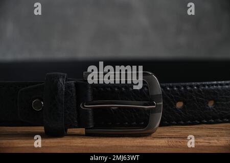 Men black leather belt with metal buckle wooden table and on gray wall background Stock Photo