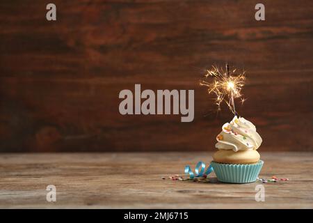 Birthday cupcake with sparkler on wooden table. Space for text Stock Photo