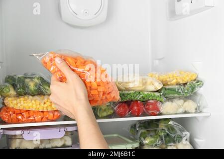 https://l450v.alamy.com/450v/2mj6b1c/woman-putting-plastic-bag-with-carrot-in-refrigerator-with-frozen-vegetables-closeup-2mj6b1c.jpg