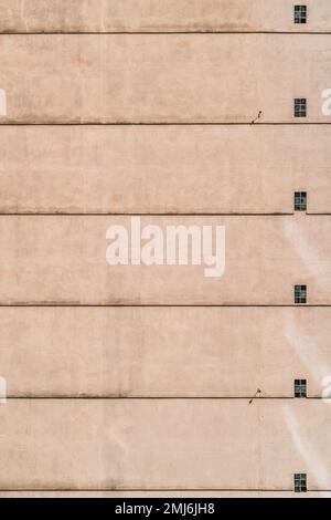 A vertical shot of a residential building wall with a sequence of small windows and floor separation lines on the plastered facade; a seamless texture Stock Photo