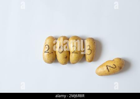 Four raw potatoes with the numbers 2023 and next to them lies a potato with the number 2, written in black felt-tip pen, lie on a white background, ve Stock Photo
