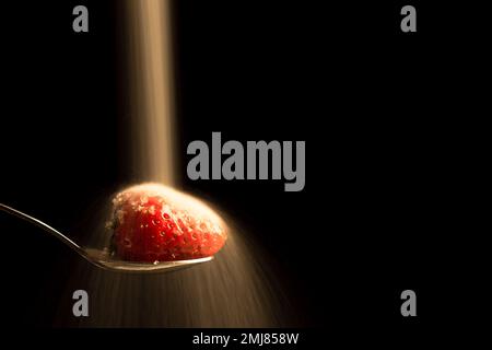 Sugar being poured on a strawberry with a dark  background, copy space on black. (horizontal format) Stock Photo