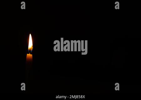 One light of a candle burning and glowing brightly against a black background, copy space on the right. Stock Photo