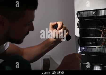 Electrician with flashlight fixing refrigerator indoors, closeup Stock Photo