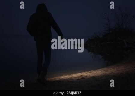 Man with flashlight walking near river in evening Stock Photo