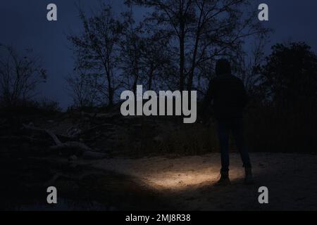 Man with flashlight walking near river in evening Stock Photo