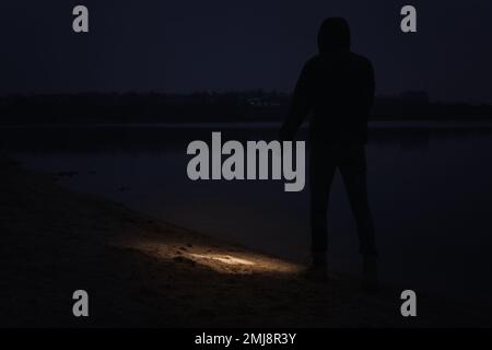Man with flashlight walking near river at night Stock Photo