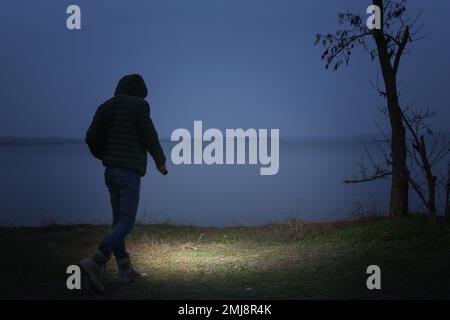 Man with flashlight walking near river in evening Stock Photo