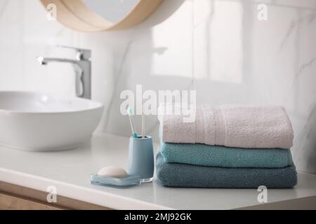 Stack of fresh towels, toothbrushes and soap bar on countertop in bathroom Stock Photo