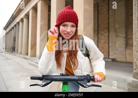 Smiling redhead european girl drives public e-scooter, tourist explores city, rides in city centre Stock Photo