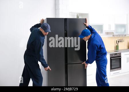 Professional workers carrying modern refrigerator in kitchen Stock Photo